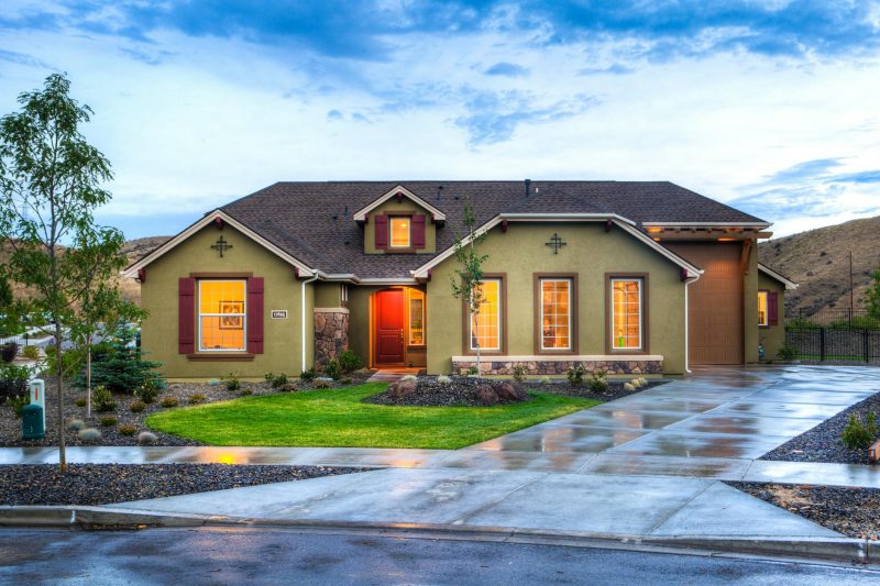 Modern home exterior with bright lighting, a green lawn, and a wet driveway.