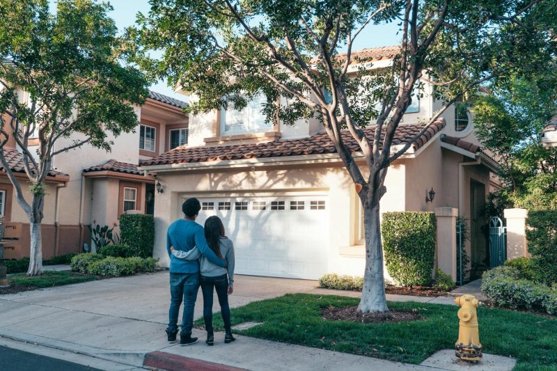 Couple hugging joyfully outside their new suburban home, symbolizing togetherness and new beginnings.