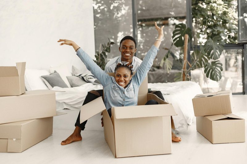 Joyful couple playfully poses in their new home, surrounded by unpacked boxes and a bright, welcoming space.