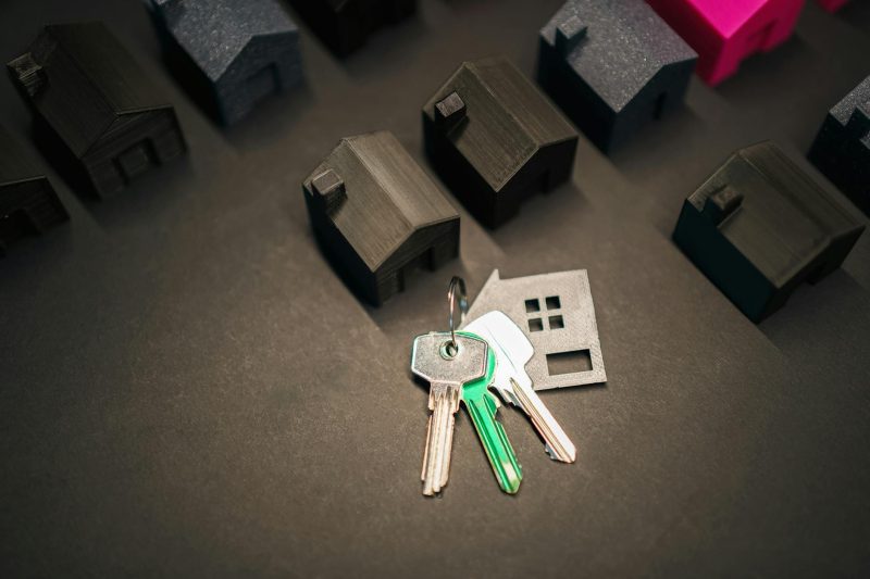 Miniature house models and a set of keys arranged on a wooden surface.