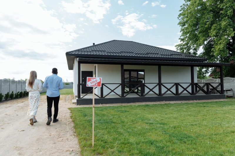 A couple walks toward their new home with a "Sold" sign in the yard.