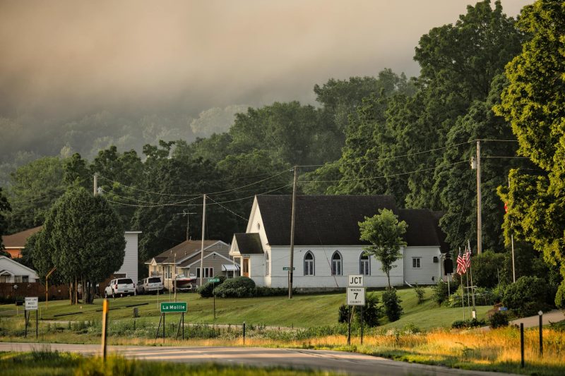 Foggy morning in Dakota, MN, featuring quaint small town architecture surrounded by lush green trees.