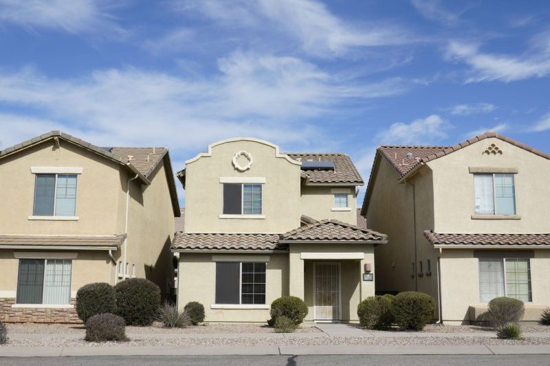 Three adjacent suburban houses in Tucson, Arizona, under a clear blue sky.