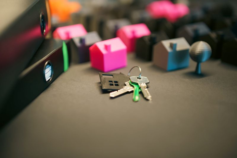 Miniature model houses and house keys arranged on a wooden desk.