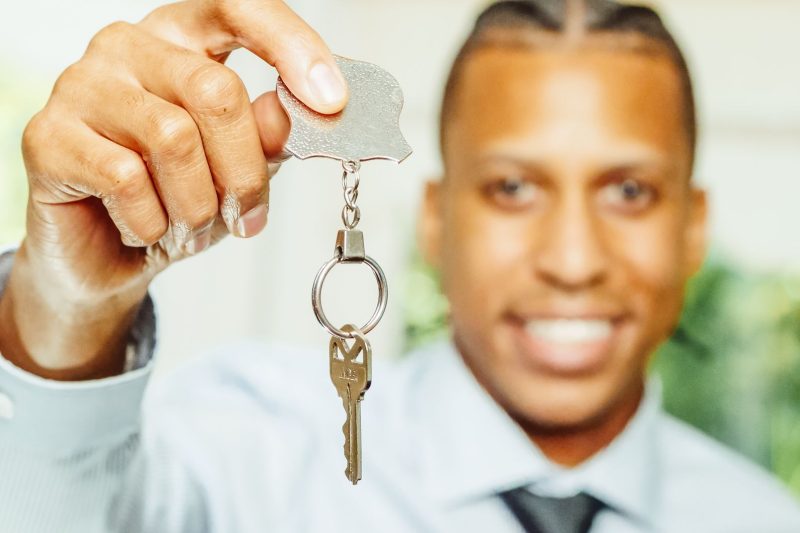 A smiling real estate agent holds up a house key, representing a successful home purchase.