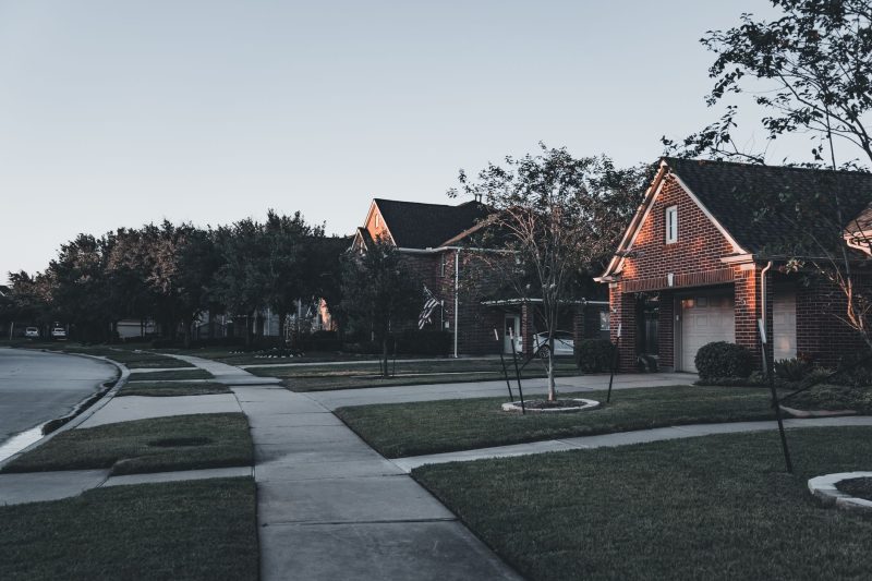 Serene suburban scene with brick houses and landscaped lawns illuminated by dusk.