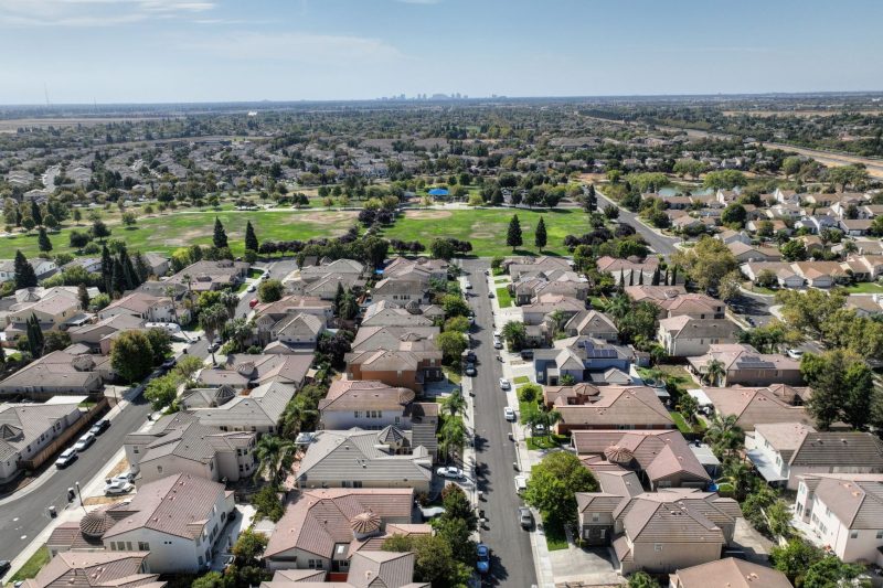 Aerial view of Sacramento suburb featuring rows of houses amidst lush greenery on a sunny day.