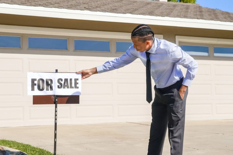 Real estate agent placing a for sale sign in front of a house on a sunny day.