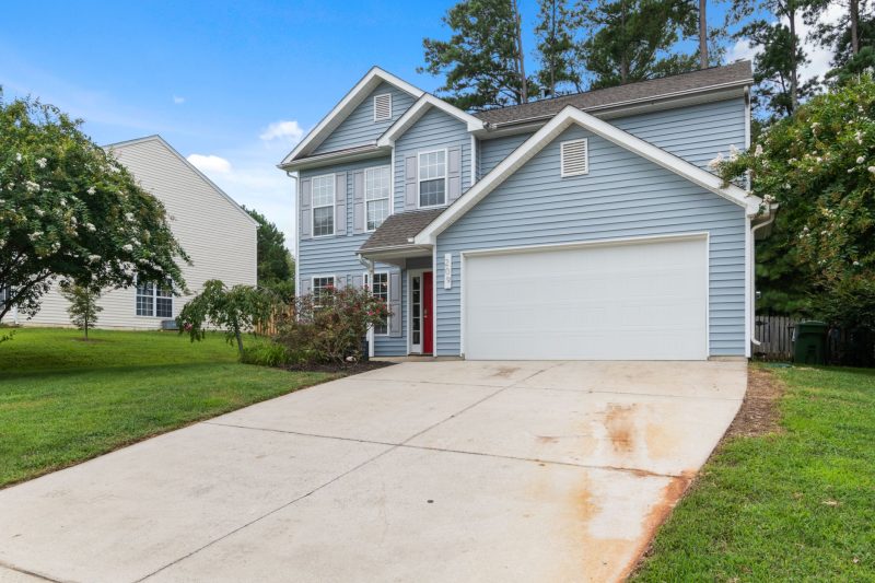 Charming two-story suburban house with a spacious driveway surrounded by greenery.
